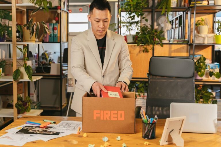 An adult man pack personal items after receiving a fired notice in an office setting, expressing corporate life challenges.